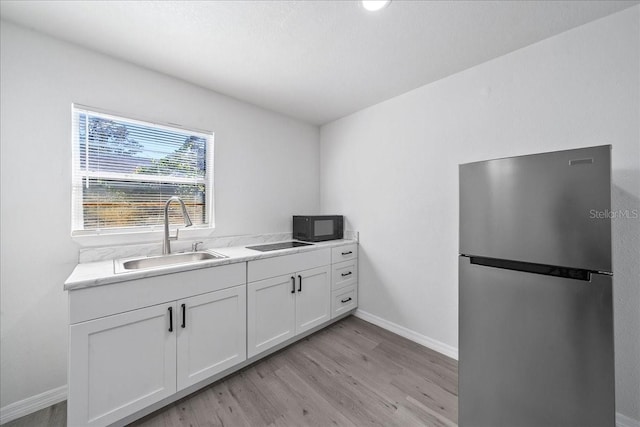 kitchen with stainless steel fridge, sink, white cabinets, and light hardwood / wood-style floors