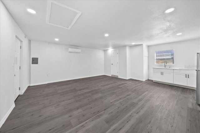 unfurnished living room with electric panel, a wall unit AC, dark wood-type flooring, and sink