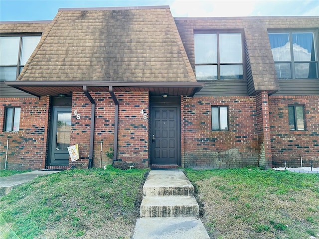 view of property with brick siding, mansard roof, and roof with shingles