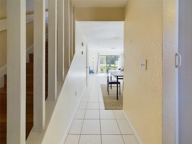 hall featuring light tile patterned floors, a textured wall, and baseboards