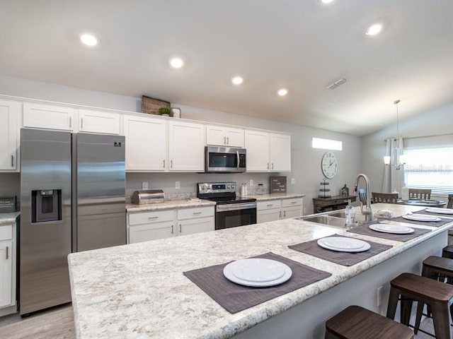 kitchen with a kitchen bar, appliances with stainless steel finishes, sink, white cabinetry, and lofted ceiling