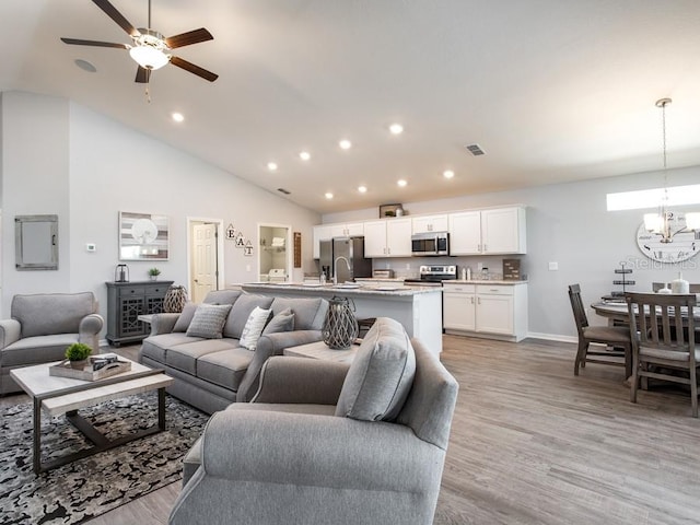 living room featuring sink, high vaulted ceiling, ceiling fan with notable chandelier, and light wood-type flooring