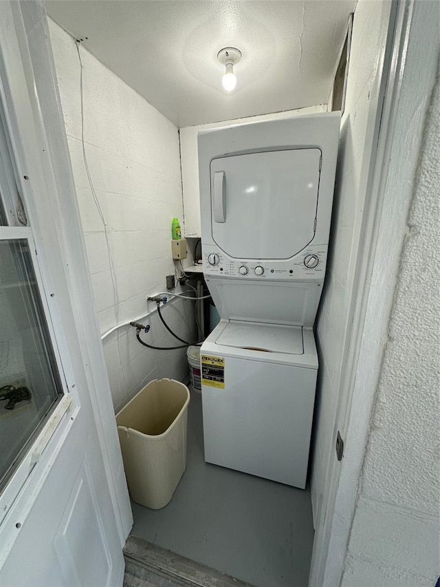 clothes washing area with stacked washer / drying machine and a textured ceiling