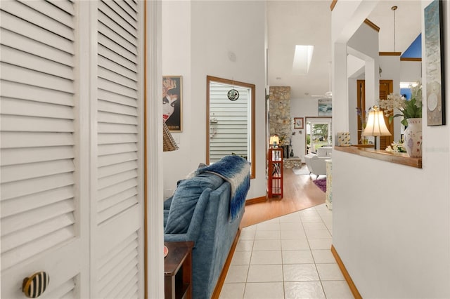 hall featuring light tile patterned floors, a skylight, and high vaulted ceiling