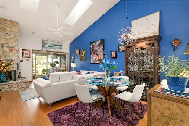 dining area with ceiling fan with notable chandelier, wood-type flooring, high vaulted ceiling, and a skylight