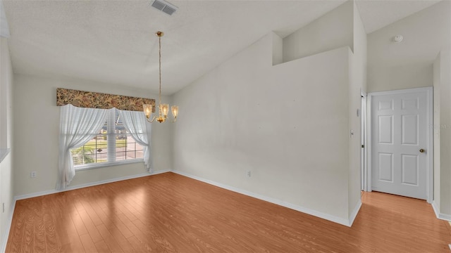 empty room with a chandelier, high vaulted ceiling, light hardwood / wood-style floors, and a textured ceiling