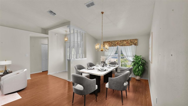 dining area with a chandelier, vaulted ceiling, and hardwood / wood-style flooring