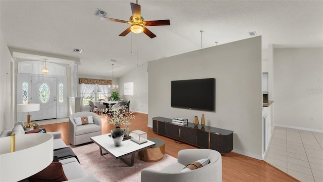 tiled living room with ceiling fan with notable chandelier, lofted ceiling, and a textured ceiling