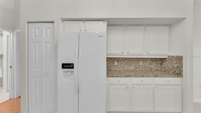 kitchen with white cabinets, light hardwood / wood-style flooring, decorative backsplash, white fridge with ice dispenser, and light stone counters