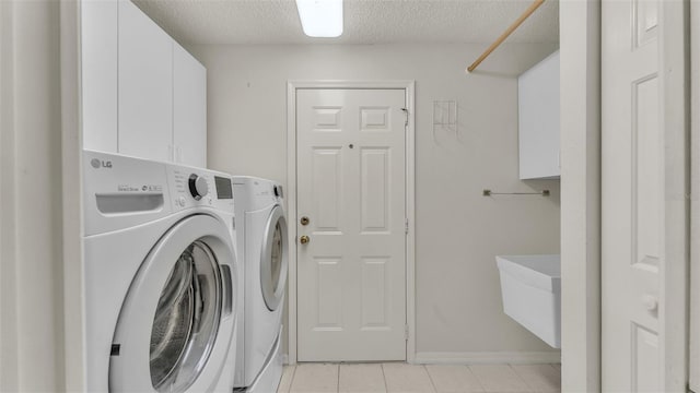 washroom featuring washing machine and dryer, light tile patterned flooring, cabinets, and a textured ceiling