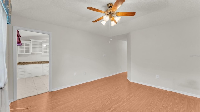 empty room with ceiling fan, a textured ceiling, and light hardwood / wood-style flooring