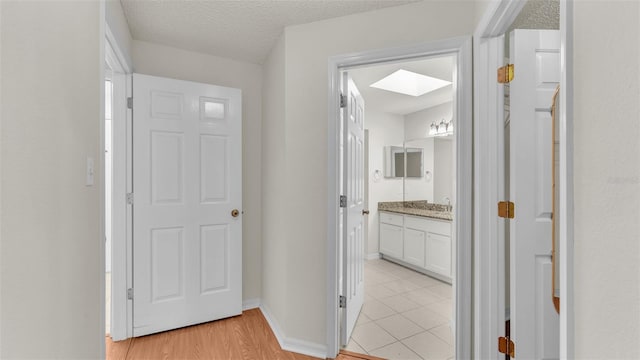 hall featuring light wood-type flooring, a textured ceiling, and a skylight