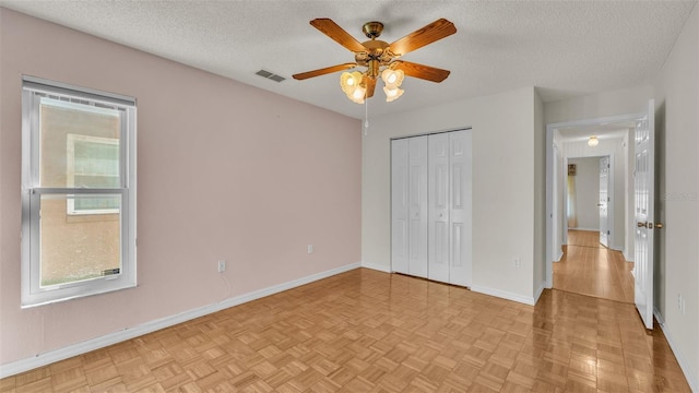 unfurnished bedroom with ceiling fan, a closet, light parquet floors, and a textured ceiling