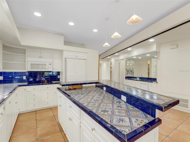 kitchen featuring decorative backsplash, tile countertops, white cabinets, a center island, and hanging light fixtures