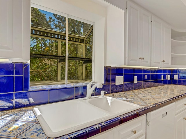 kitchen with tile countertops, backsplash, white dishwasher, sink, and white cabinetry