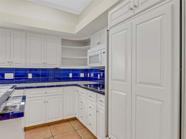 kitchen with light tile patterned floors, tasteful backsplash, cooktop, tile countertops, and white cabinets