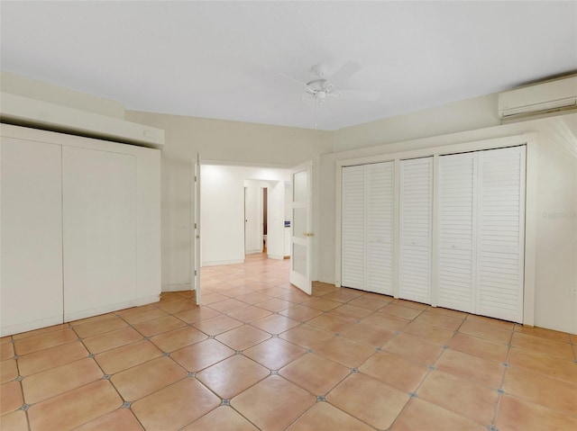 unfurnished bedroom with light tile patterned floors, two closets, an AC wall unit, and ceiling fan