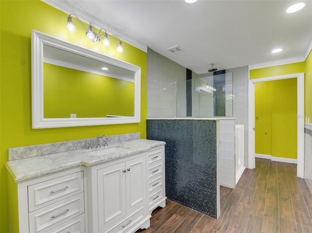 bathroom featuring vanity, wood-type flooring, ornamental molding, and tiled shower