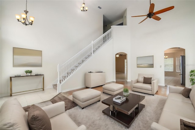 living room with a high ceiling, ceiling fan with notable chandelier, and light tile patterned floors