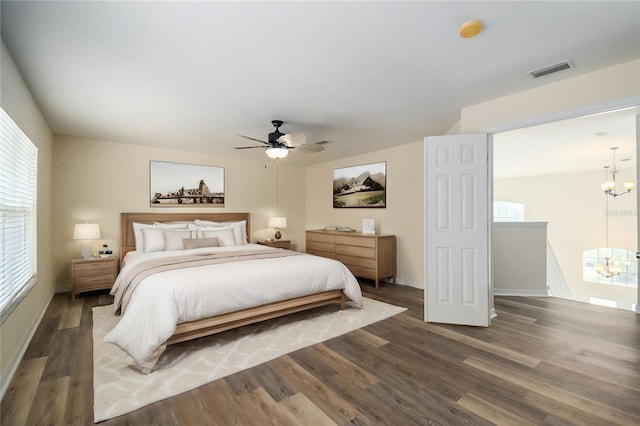 bedroom with ceiling fan with notable chandelier and dark hardwood / wood-style floors