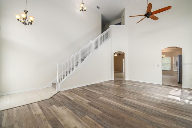 unfurnished living room with ceiling fan with notable chandelier, a towering ceiling, and light hardwood / wood-style flooring