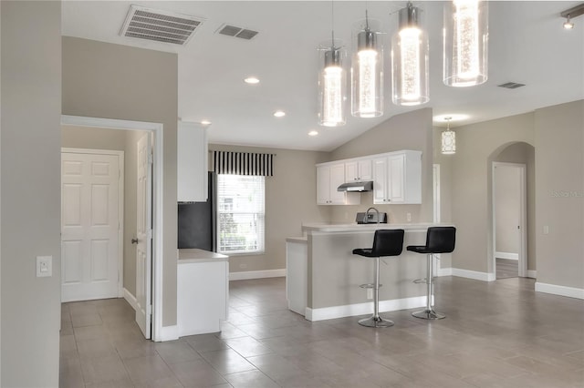 kitchen with white cabinets, a kitchen breakfast bar, vaulted ceiling, and hanging light fixtures