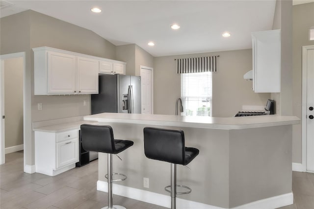 kitchen with white cabinets, a breakfast bar, appliances with stainless steel finishes, and vaulted ceiling