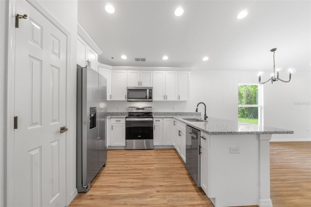 kitchen with white cabinets, hanging light fixtures, sink, light hardwood / wood-style flooring, and appliances with stainless steel finishes