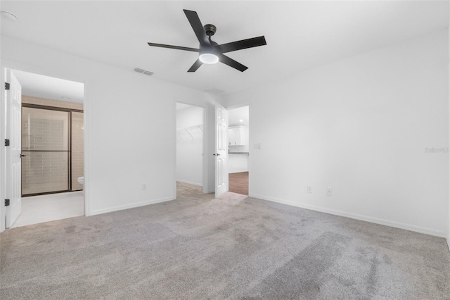 unfurnished bedroom featuring ensuite bath, light colored carpet, ceiling fan, a spacious closet, and a closet