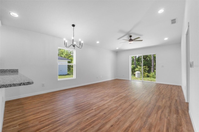 unfurnished living room featuring ceiling fan with notable chandelier, dark wood-type flooring, and a wealth of natural light