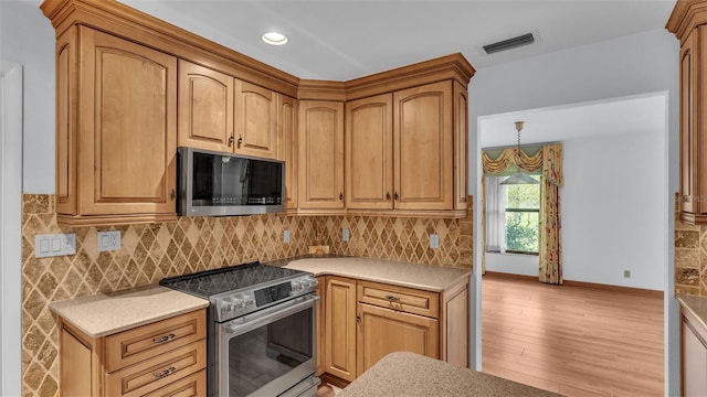 kitchen with backsplash, decorative light fixtures, light wood-type flooring, and stainless steel appliances