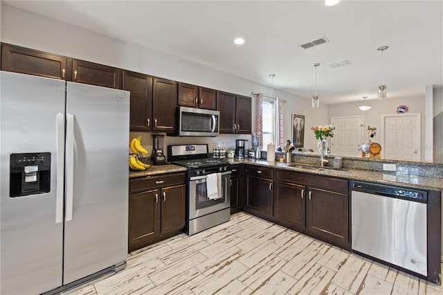 kitchen with sink, light stone counters, kitchen peninsula, decorative light fixtures, and appliances with stainless steel finishes