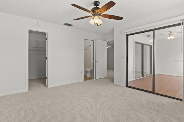 unfurnished bedroom featuring connected bathroom, ceiling fan, a spacious closet, a textured ceiling, and light carpet