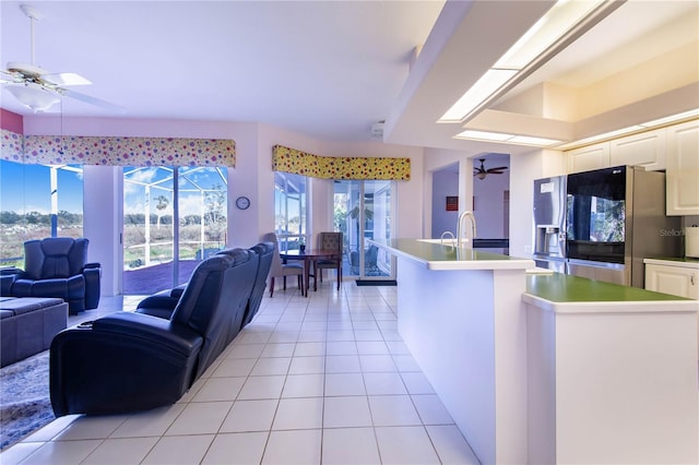 kitchen with a kitchen island with sink, ceiling fan, light tile patterned floors, stainless steel fridge with ice dispenser, and white cabinetry