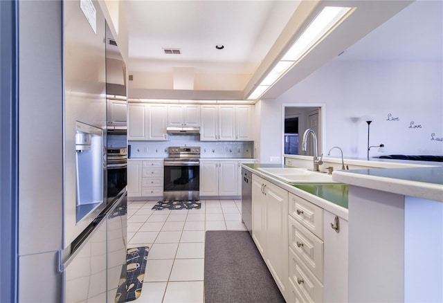 kitchen with white cabinets, sink, light tile patterned floors, tasteful backsplash, and stainless steel appliances