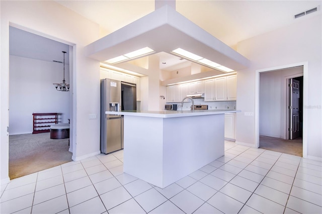 kitchen featuring stainless steel appliances, light colored carpet, a chandelier, white cabinetry, and an island with sink