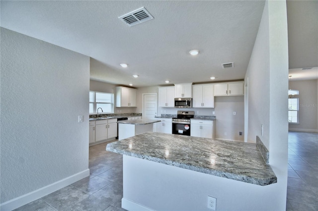 kitchen with white cabinetry, light stone countertops, stainless steel appliances, and sink