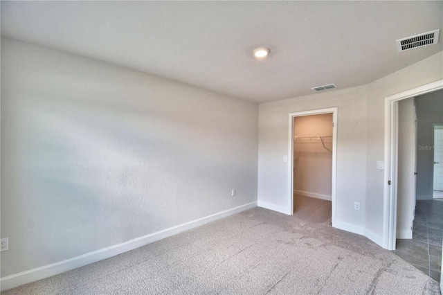 unfurnished bedroom with a walk in closet, a closet, and dark colored carpet