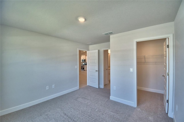 unfurnished bedroom featuring a walk in closet, baseboards, visible vents, and carpet