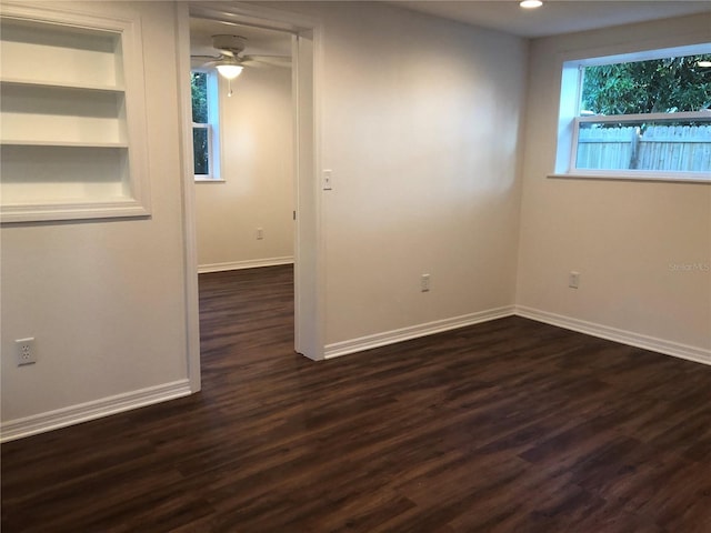 empty room featuring built in shelves, ceiling fan, and dark hardwood / wood-style flooring