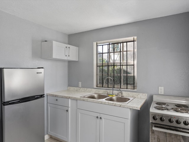 kitchen with sink, stainless steel fridge, white cabinetry, range with electric stovetop, and a textured ceiling