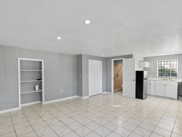 unfurnished living room featuring sink, built in shelves, and a textured ceiling