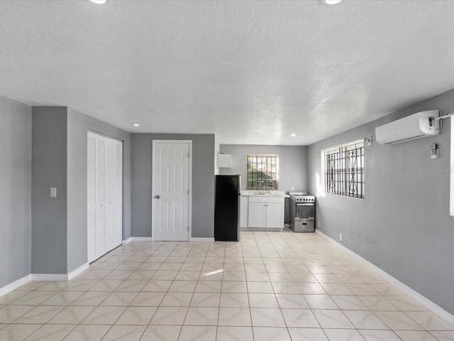 interior space with sink, appliances with stainless steel finishes, a wall unit AC, a textured ceiling, and white cabinets