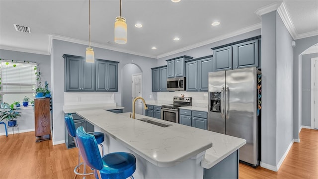 kitchen featuring sink, appliances with stainless steel finishes, light stone countertops, an island with sink, and decorative light fixtures