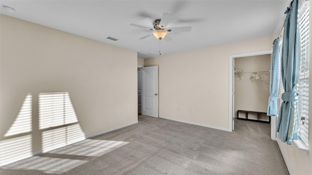 unfurnished bedroom with light carpet, a walk in closet, a closet, and ceiling fan