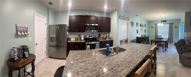 kitchen with dark brown cabinetry, light stone countertops, hanging light fixtures, a kitchen island with sink, and appliances with stainless steel finishes