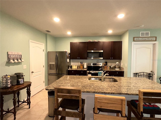 kitchen with a kitchen island with sink, sink, appliances with stainless steel finishes, dark brown cabinets, and light tile patterned flooring