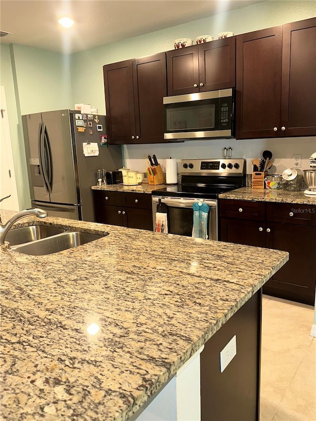 kitchen with light stone countertops, sink, stainless steel appliances, dark brown cabinets, and light tile patterned flooring