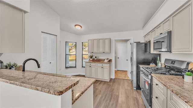 kitchen with light stone countertops, kitchen peninsula, a textured ceiling, stainless steel appliances, and light hardwood / wood-style floors