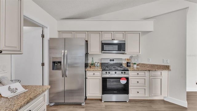 kitchen featuring appliances with stainless steel finishes, light stone counters, a textured ceiling, vaulted ceiling, and light hardwood / wood-style floors